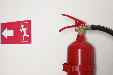 Photo of Fire extinguisher and emergency exit sign on white wall, closeup
