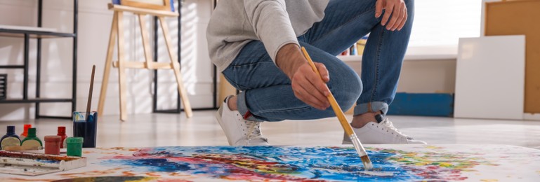 Young man painting on canvas with brush in artist studio. Banner design