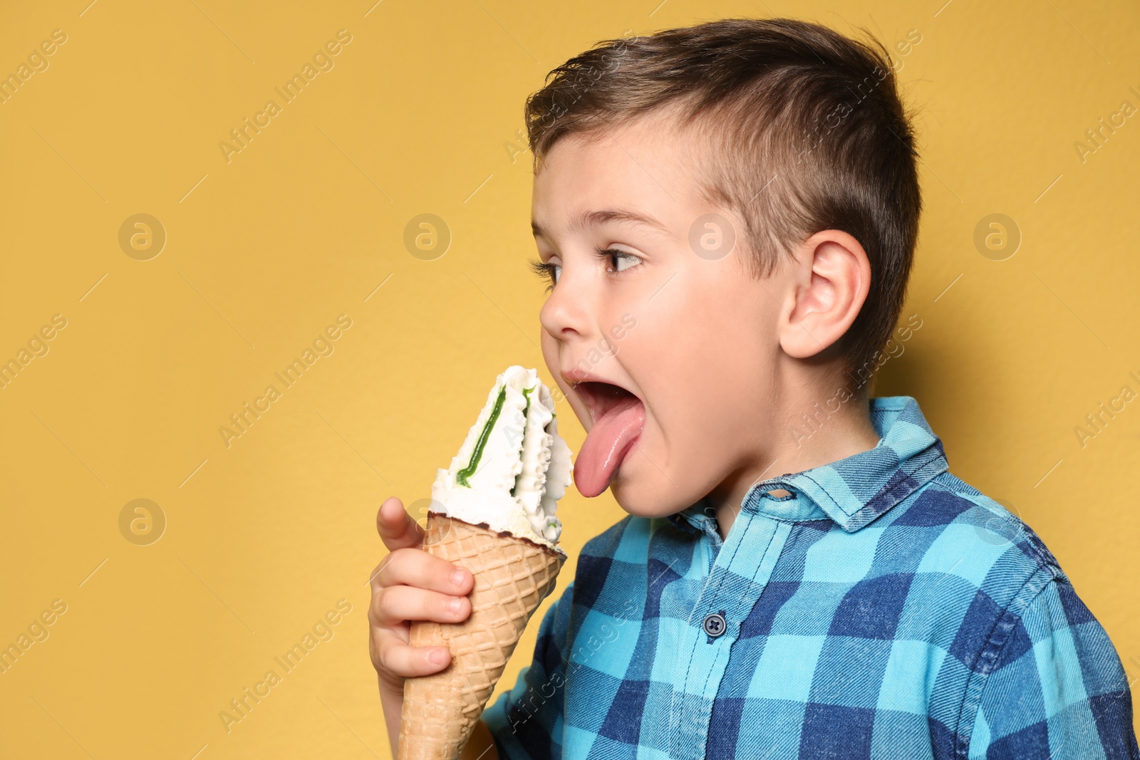 Photo of Adorable little boy with delicious ice cream against color background, space for text