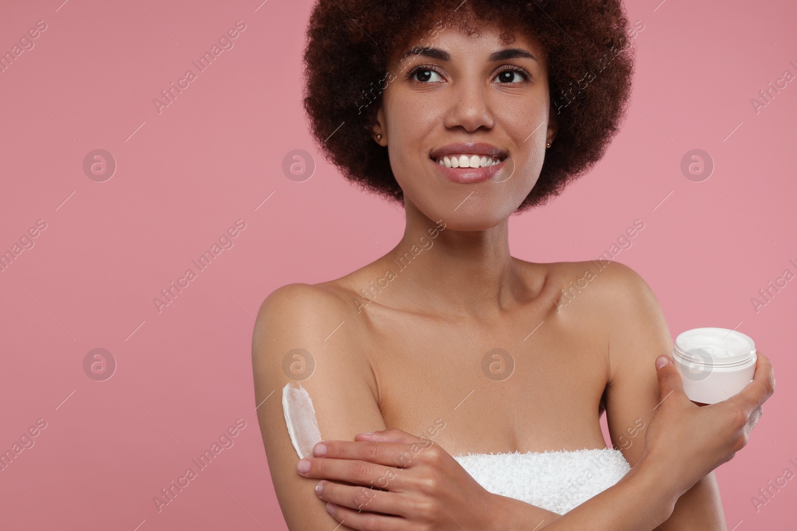 Photo of Beautiful young woman applying body cream onto arm on pink background, space for text