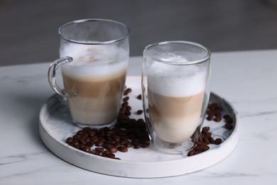 Photo of Aromatic latte macchiato and coffee beans on white marble table against blurred background, closeup