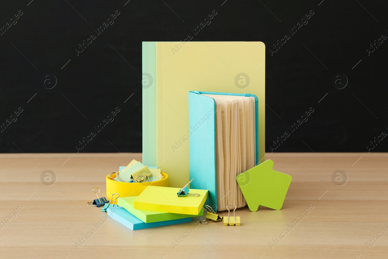 Photo of Different school stationery on wooden table near blackboard. Back to school