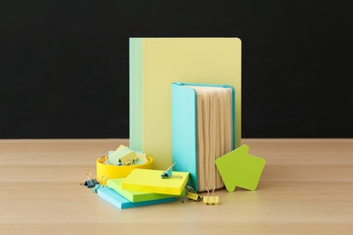 Photo of Different school stationery on wooden table near blackboard. Back to school