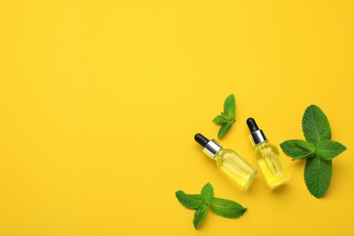 Bottles of essential oil and mint on yellow background, flat lay. Space for text