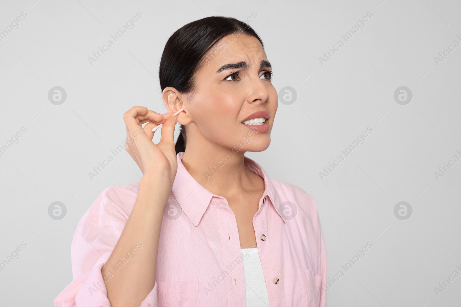 Photo of Young woman cleaning ear with cotton swab on light grey background