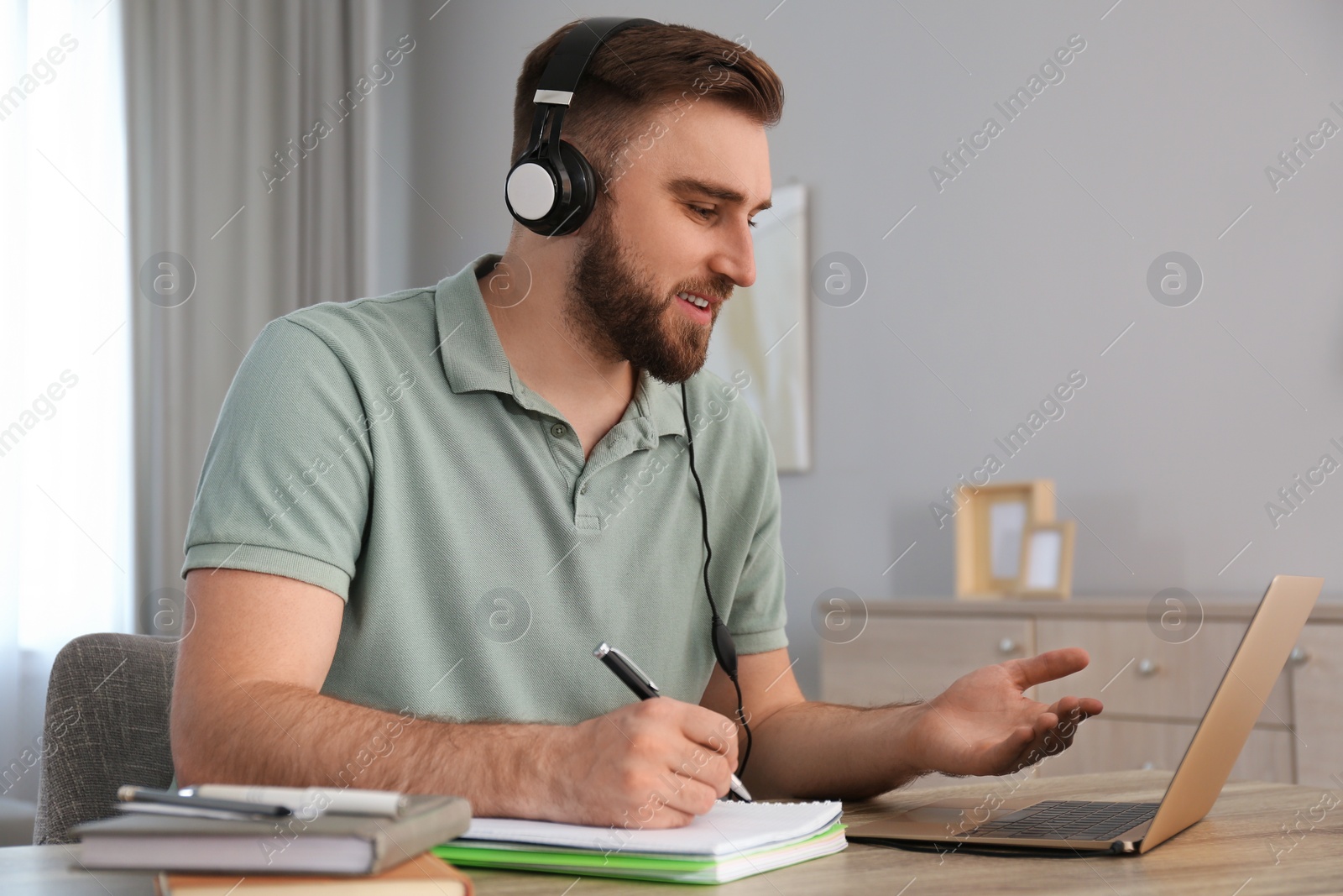 Photo of Young man taking notes during online webinar at table indoors