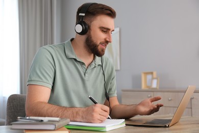 Young man taking notes during online webinar at table indoors