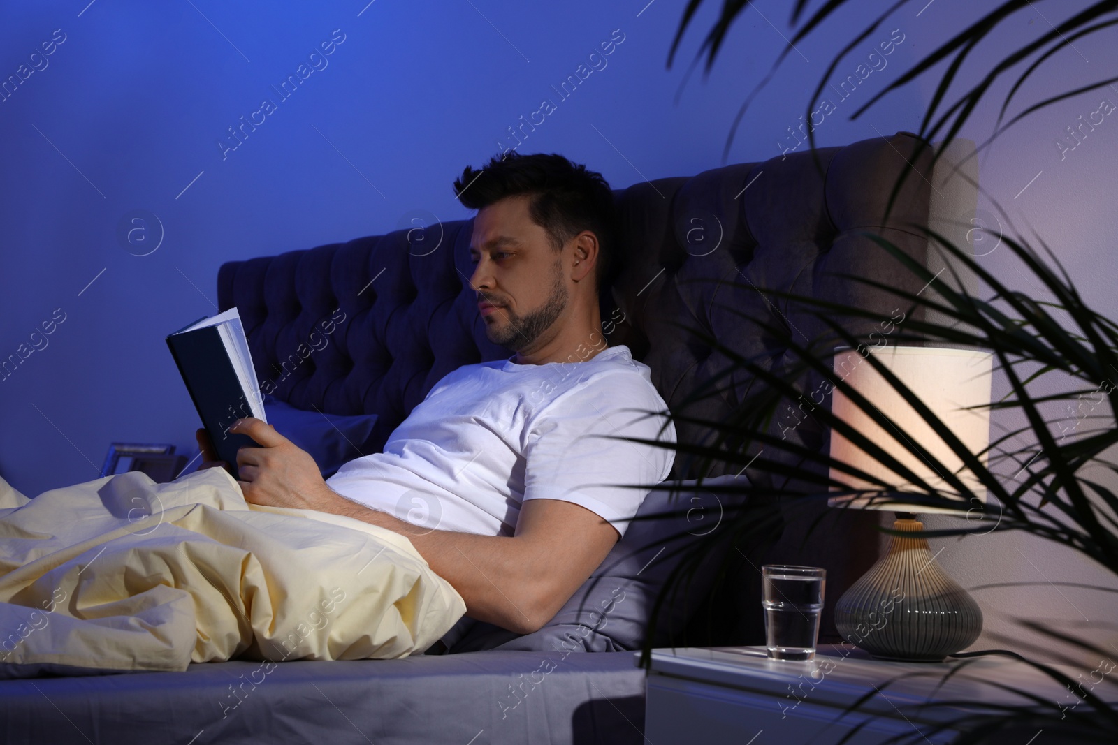 Photo of Handsome man reading book in dark room at night. Bedtime