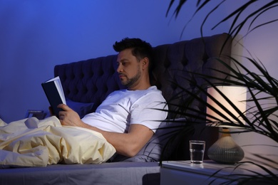 Handsome man reading book in dark room at night. Bedtime