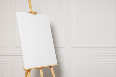 Wooden easel with blank canvas near white wall. Space for text