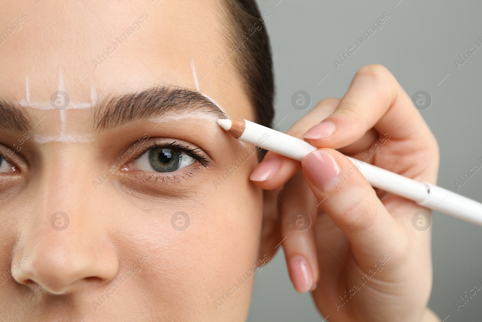 Photo of Beautician preparing young woman for procedure of permanent eyebrow makeup on grey background, closeup