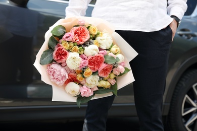 Young man with beautiful flower bouquet near car, closeup view