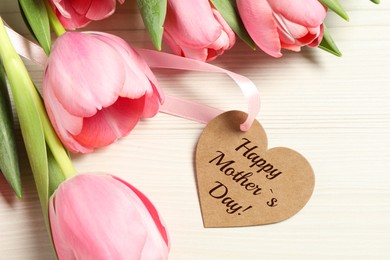 Happy Mother's Day. Heart shaped greeting label and beautiful tulip flowers on white wooden table