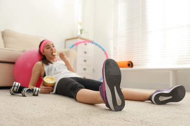 Photo of Lazy young woman eating ice cream instead of training at home, focus on legs