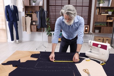 Professional tailor with measuring tape working at table in atelier, space for text