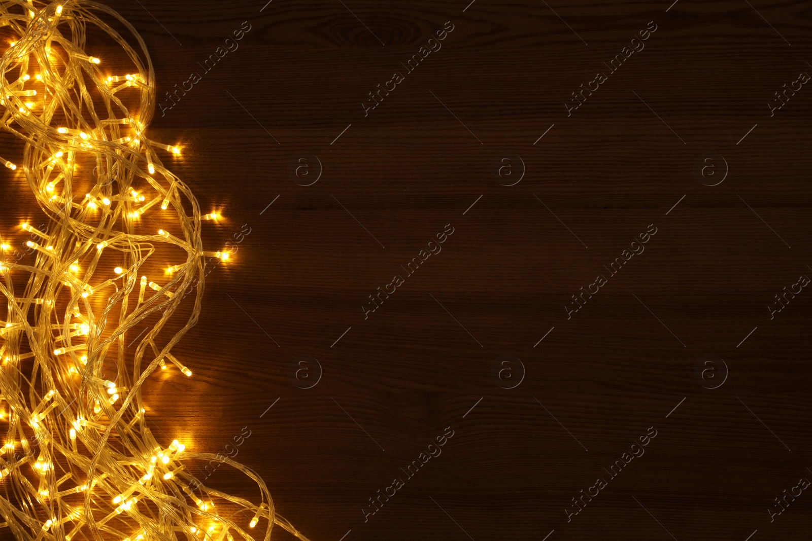 Photo of Beautiful glowing Christmas lights on wooden table, top view. Space for text