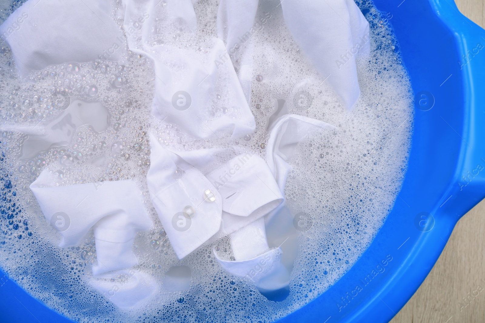 Photo of Basin with white garment in suds, top view. Hand washing laundry