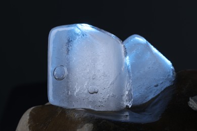 Crystal clear ice cubes on stone against dark background, closeup. Color tone effect