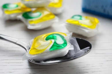 Photo of Spoon with dishwasher detergent pod on white wooden table, closeup