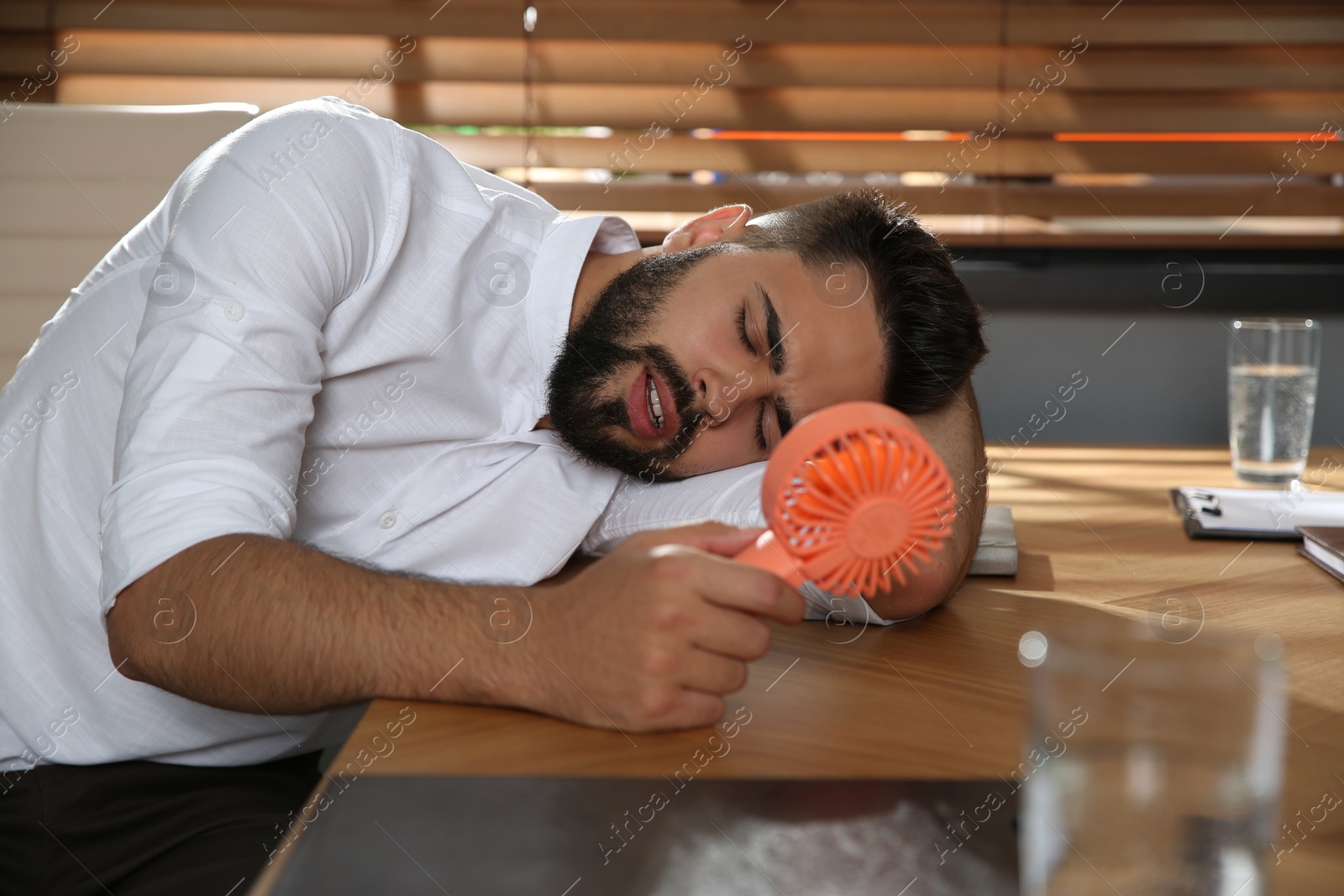 Photo of Man with portable fan suffering from heat at workplace. Summer season