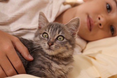 Photo of Cute little child with kitten in bed, focus on pet