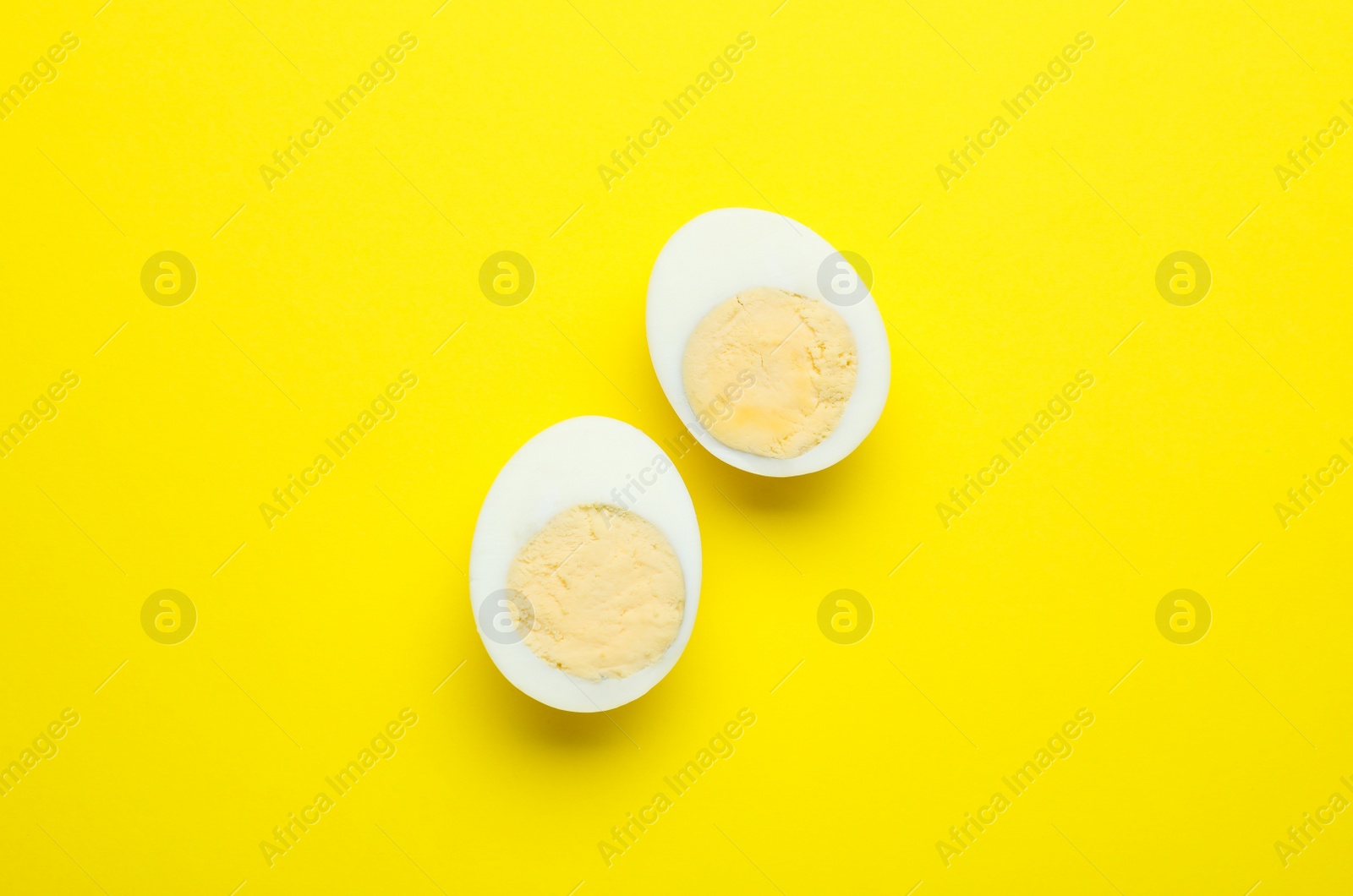 Photo of Halves of fresh hard boiled egg on yellow background, flat lay