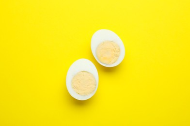 Halves of fresh hard boiled egg on yellow background, flat lay