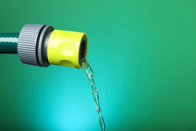 Photo of Water dripping from hose on green background, closeup. Space for text