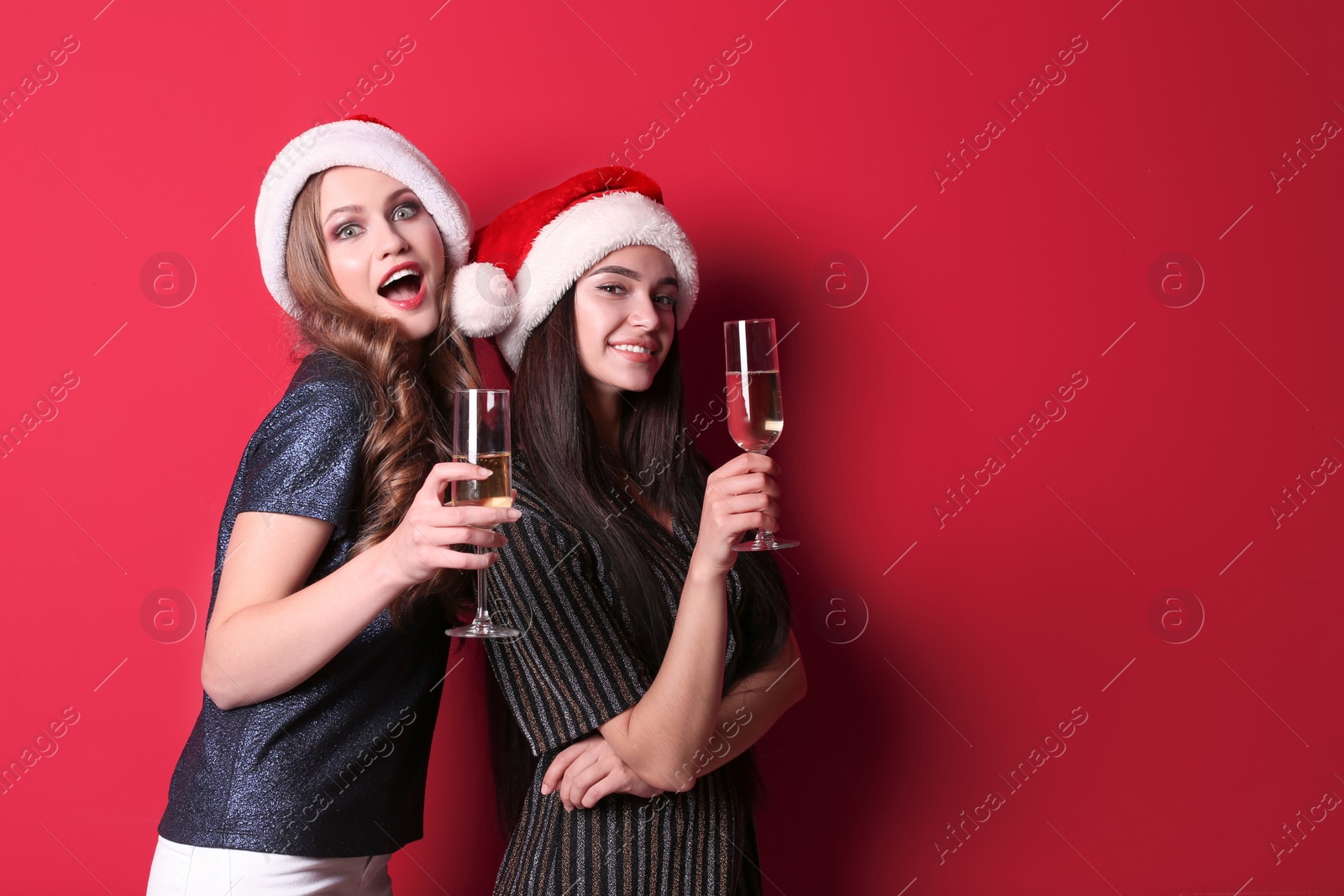 Photo of Beautiful young women in Santa hats with glasses of champagne on color background. Christmas celebration