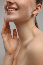 Smiling woman touching her chin on grey background, closeup