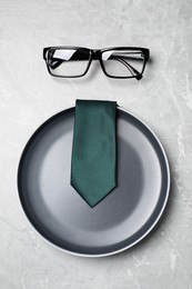 Photo of Business lunch concept. Plate, tie and glasses on light gray marble table, flat lay