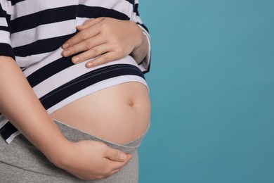 Pregnant woman on light blue background, closeup. Space for text