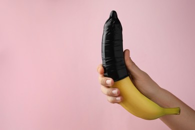 Photo of Woman holding banana in condom on pink background, closeup and space for text. Safe sex concept