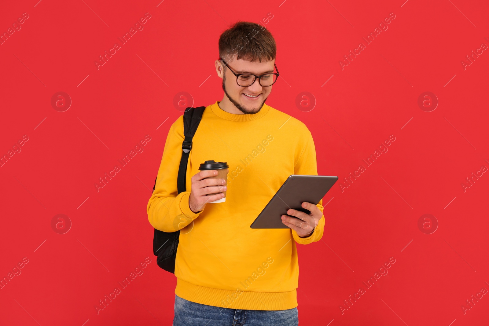 Photo of Young student with backpack, tablet and cup of coffee on red background