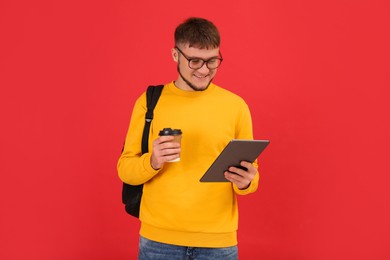 Photo of Young student with backpack, tablet and cup of coffee on red background
