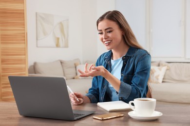 Photo of Happy woman having video chat via laptop at wooden table in room