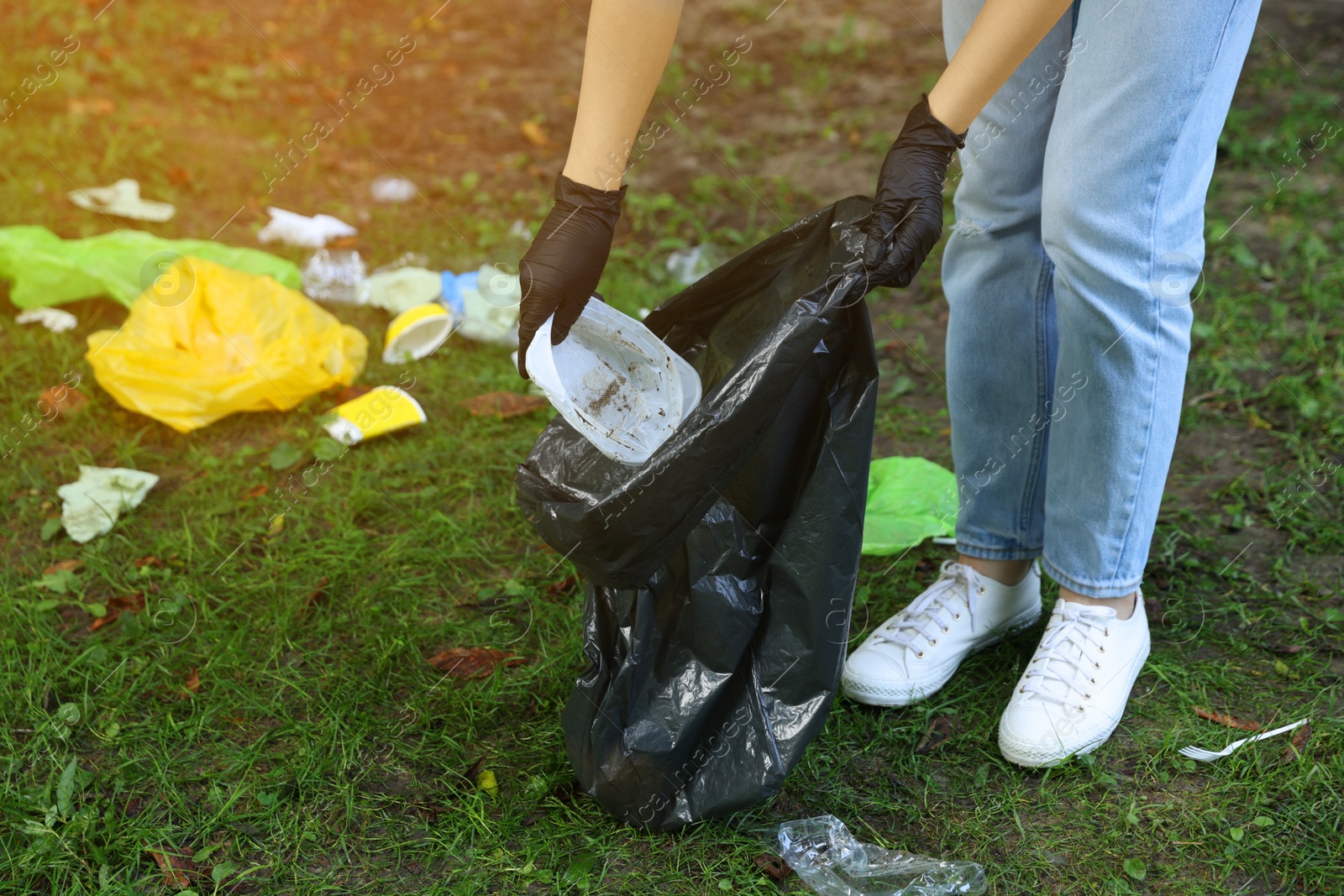 Photo of Woman with plastic bag collecting garbage on green grass, closeup