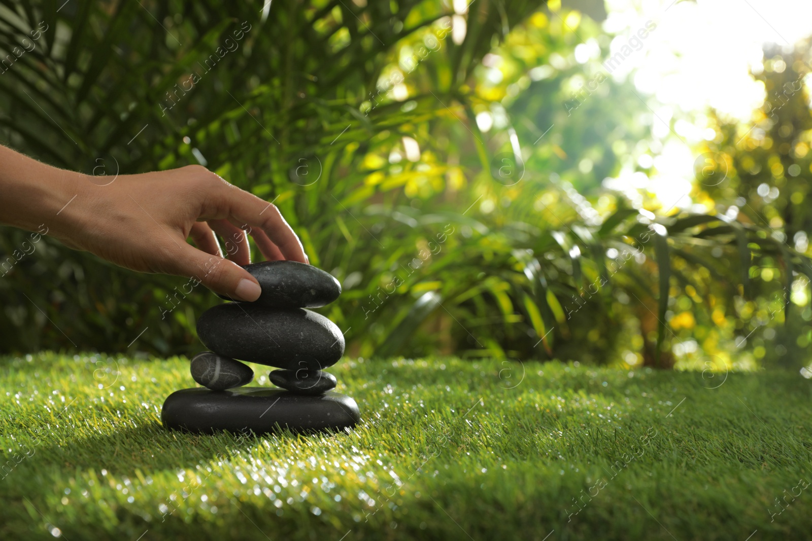 Photo of Woman stacking stones on green grass in garden, closeup. Space for text