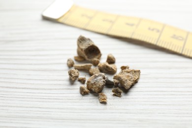Photo of Kidney stones and measuring tape on white wooden table, closeup