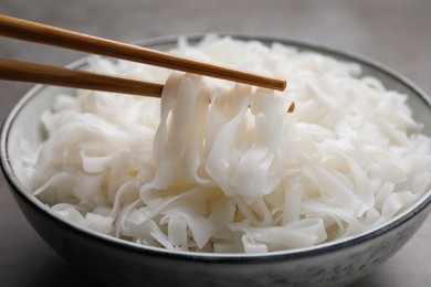 Photo of Chopsticks with cooked rice noodles over bowl on table, closeup