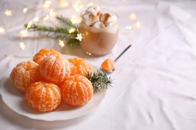 Photo of Peeled delicious ripe tangerines and glass of drink with marshmallows on white bedsheet. Space for text