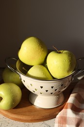 Fresh apples in colander on white table