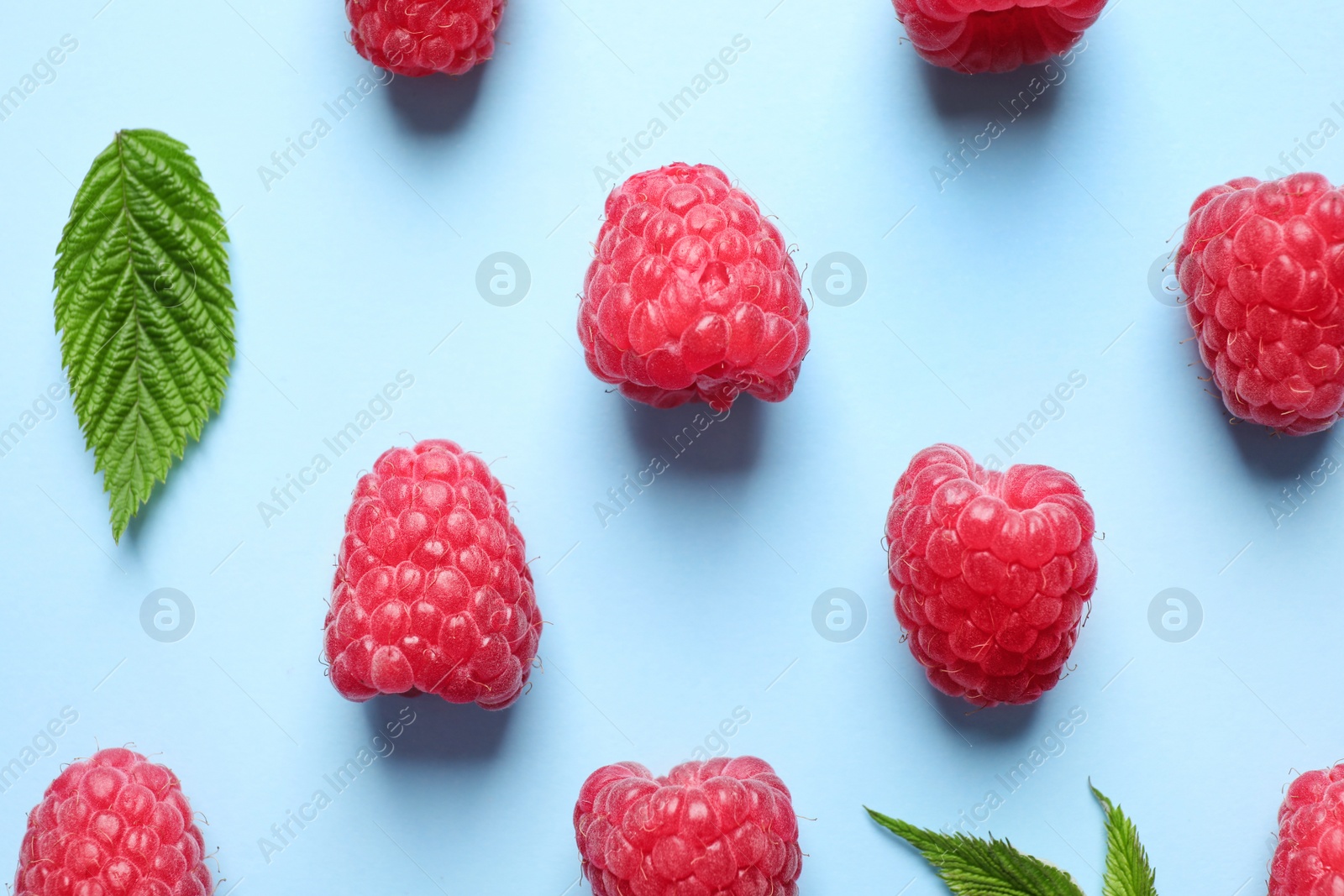 Photo of Fresh sweet ripe raspberries on light blue background, flat lay