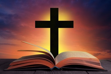 Image of Silhouette of cross and open Bible on wooden table at sunset