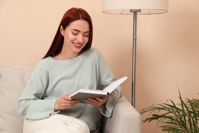 Photo of Happy woman with red dyed hair reading book at home