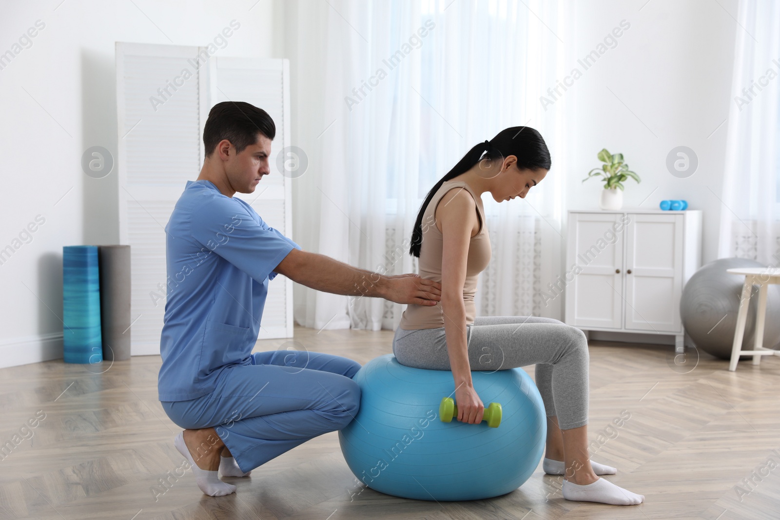 Photo of Orthopedist helping patient to do exercise with dumbbell in clinic. Scoliosis treatment