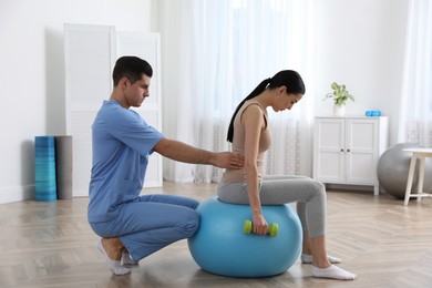 Photo of Orthopedist helping patient to do exercise with dumbbell in clinic. Scoliosis treatment