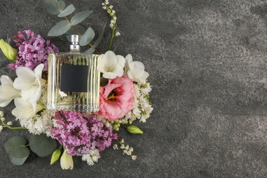 Bottle of luxury perfume and floral decor on dark grey table, top view. Space for text