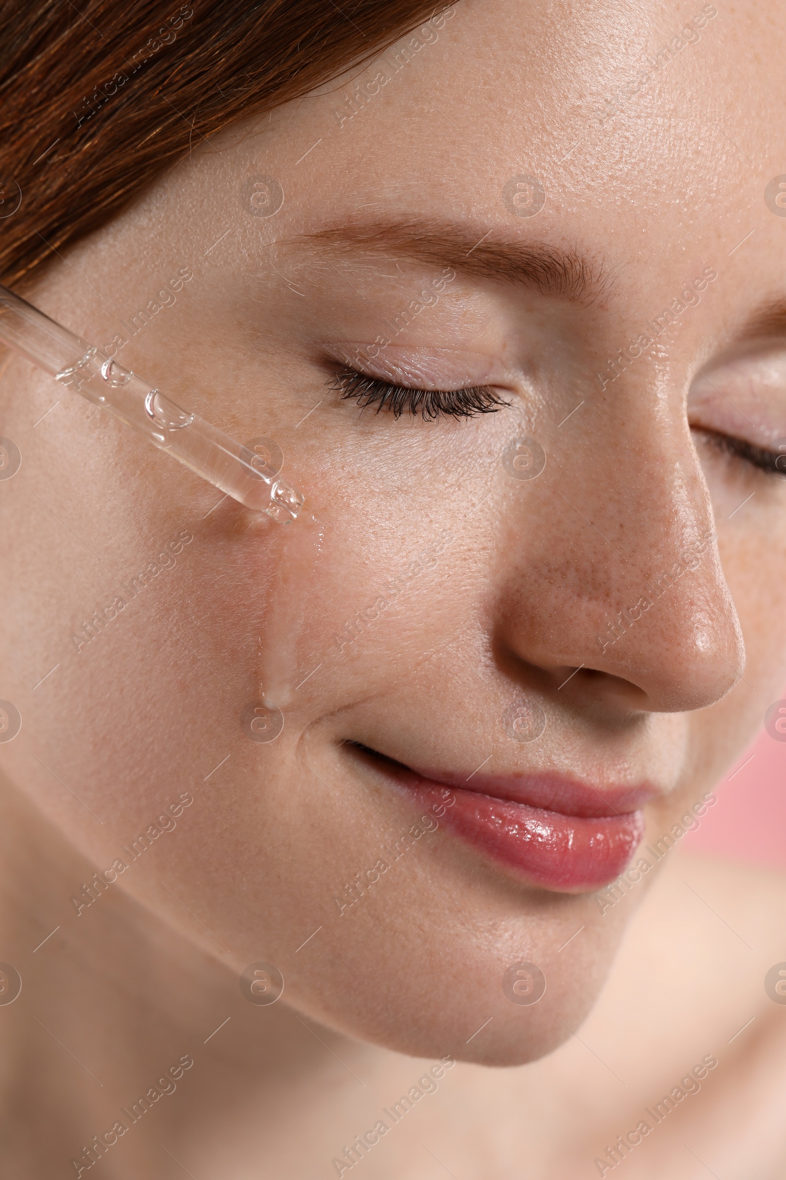 Photo of Beautiful woman with freckles applying cosmetic serum onto her face, closeup