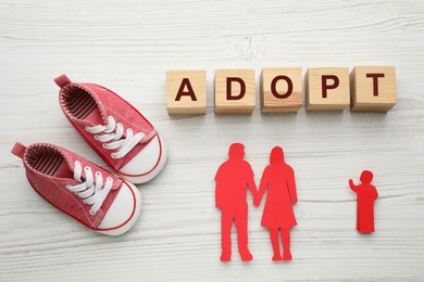 Photo of Figures of parents with child, shoes and word Adopt on white wooden table, flat lay